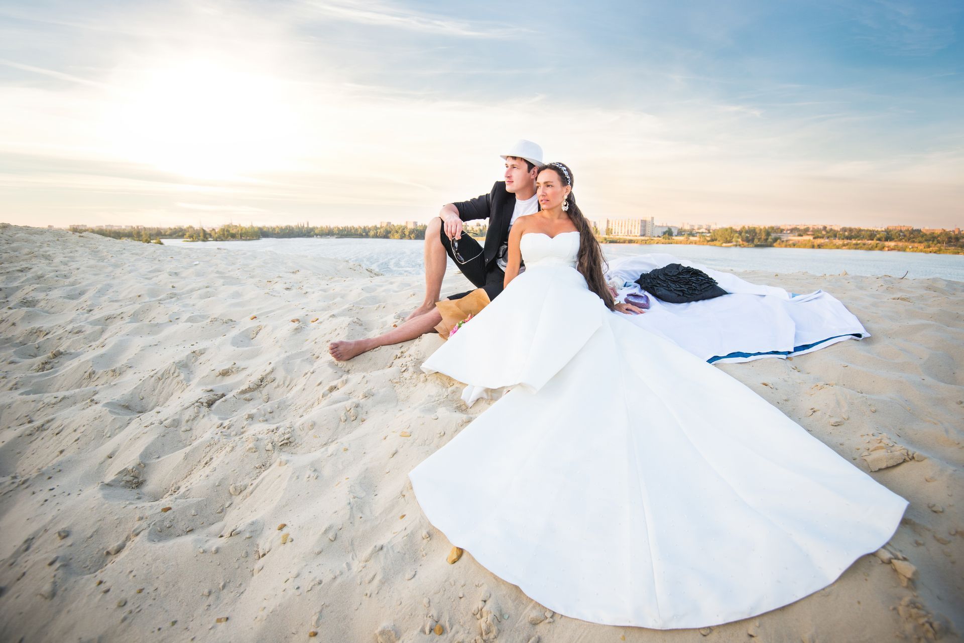 A bride and groom are sitting on a blanket on the beach.