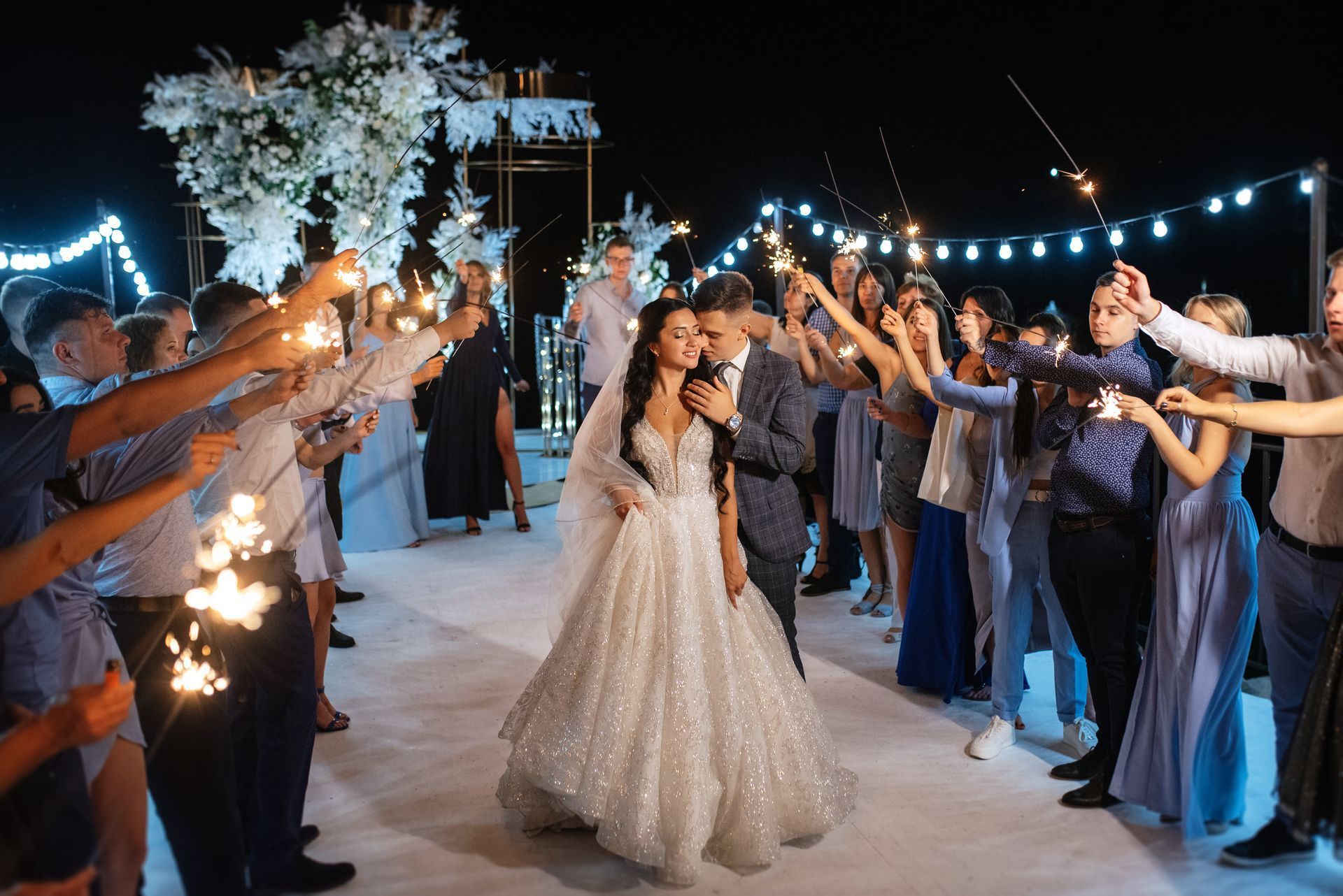 A bride and groom are walking through a tunnel of sparklers at their wedding reception.