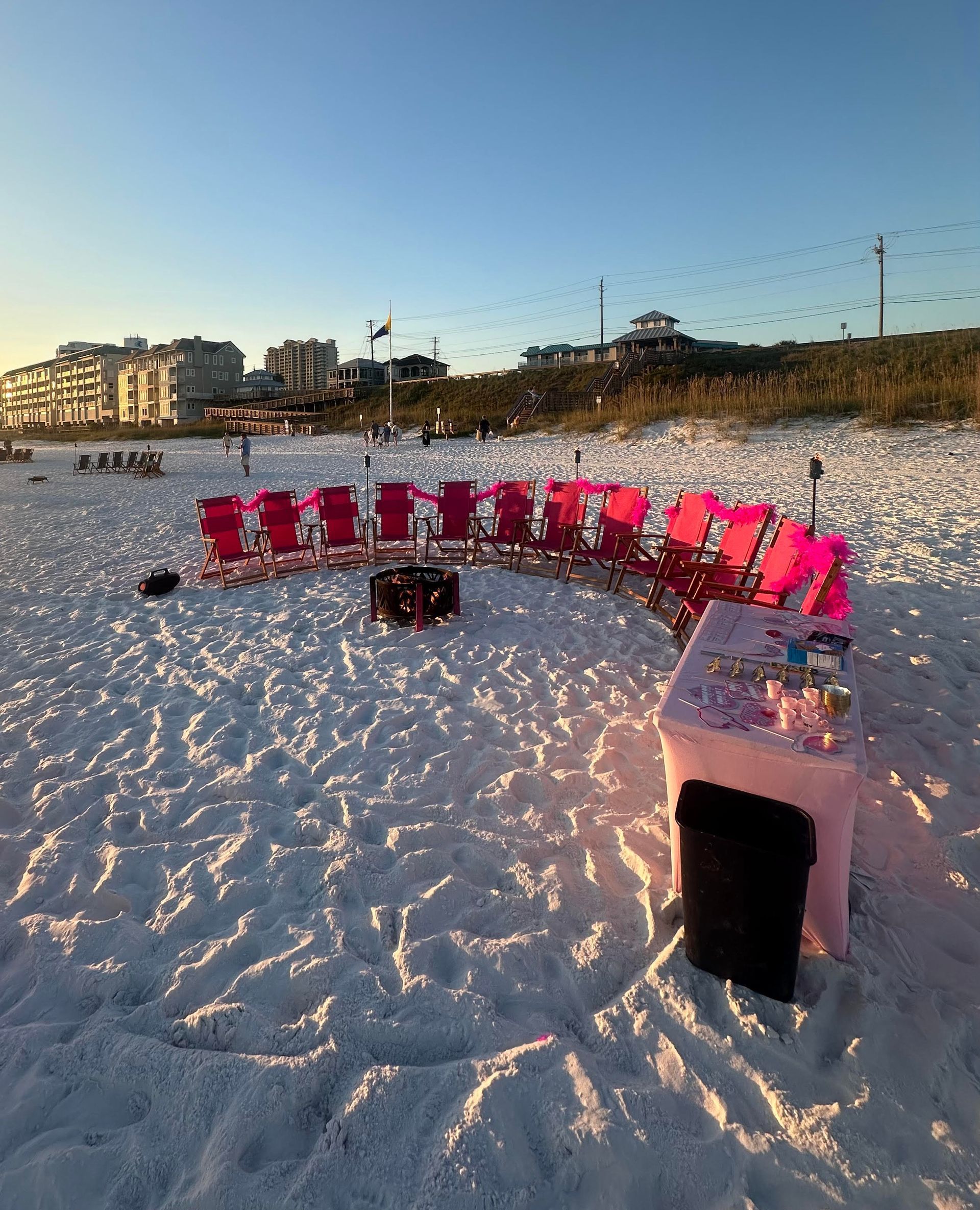 Picnic setup on a beach: flowers, pink dishes, pillows, candles on a blanket.
