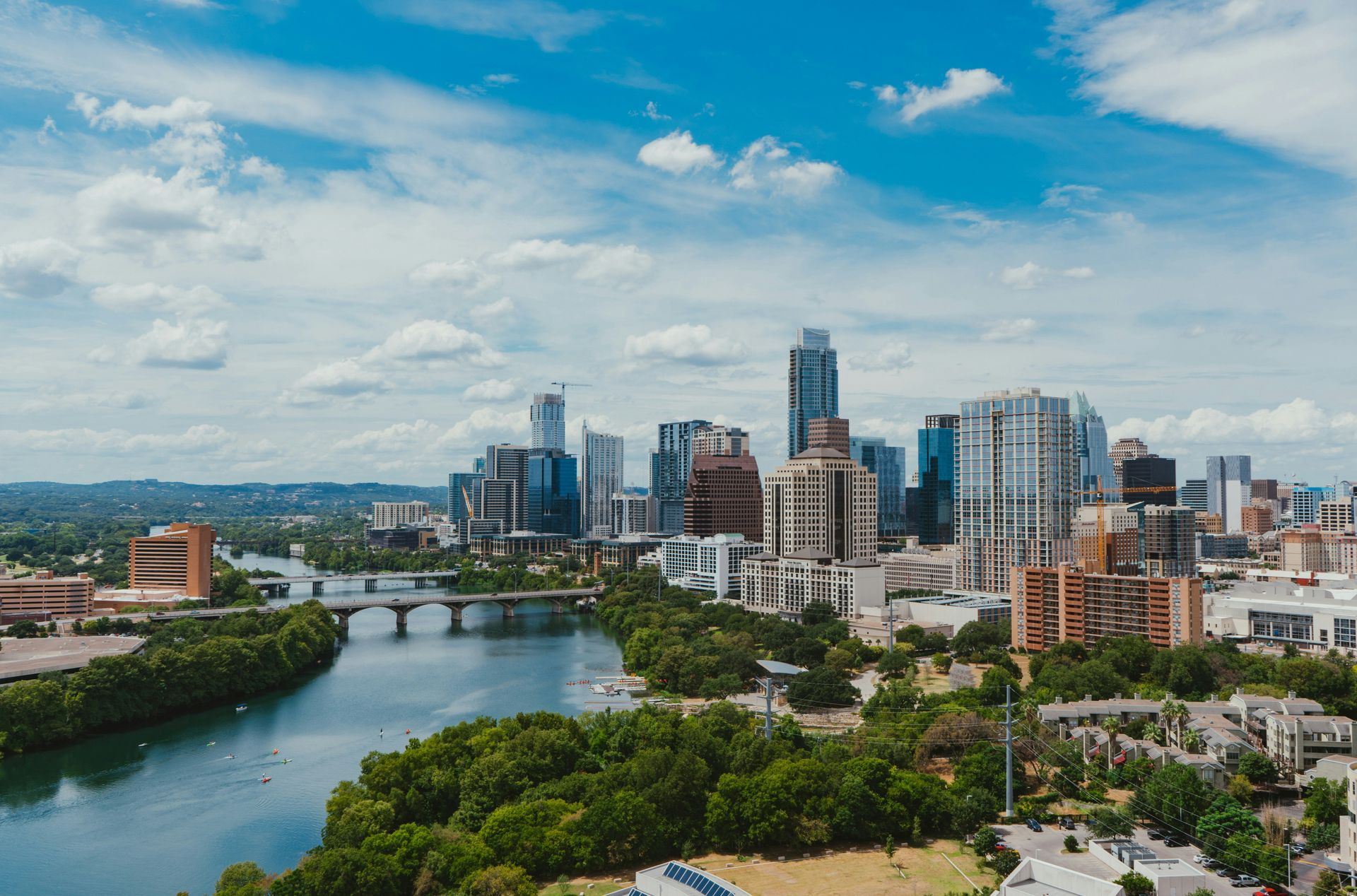City skyline beside a river under a bright blue sky with scattered clouds
