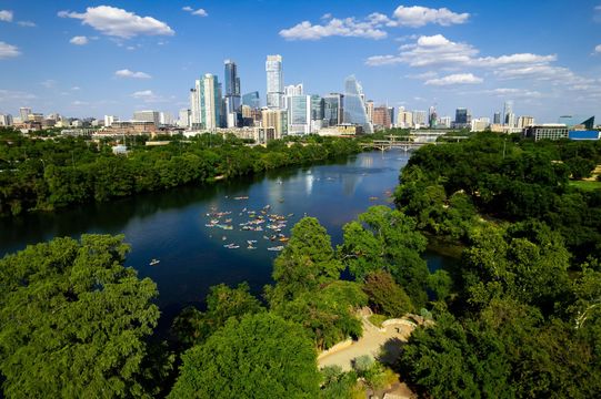 City skyline above a lush green park and river under a bright blue sky