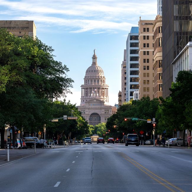 Downtown street leading to a domed capitol building framed by trees and tall buildings