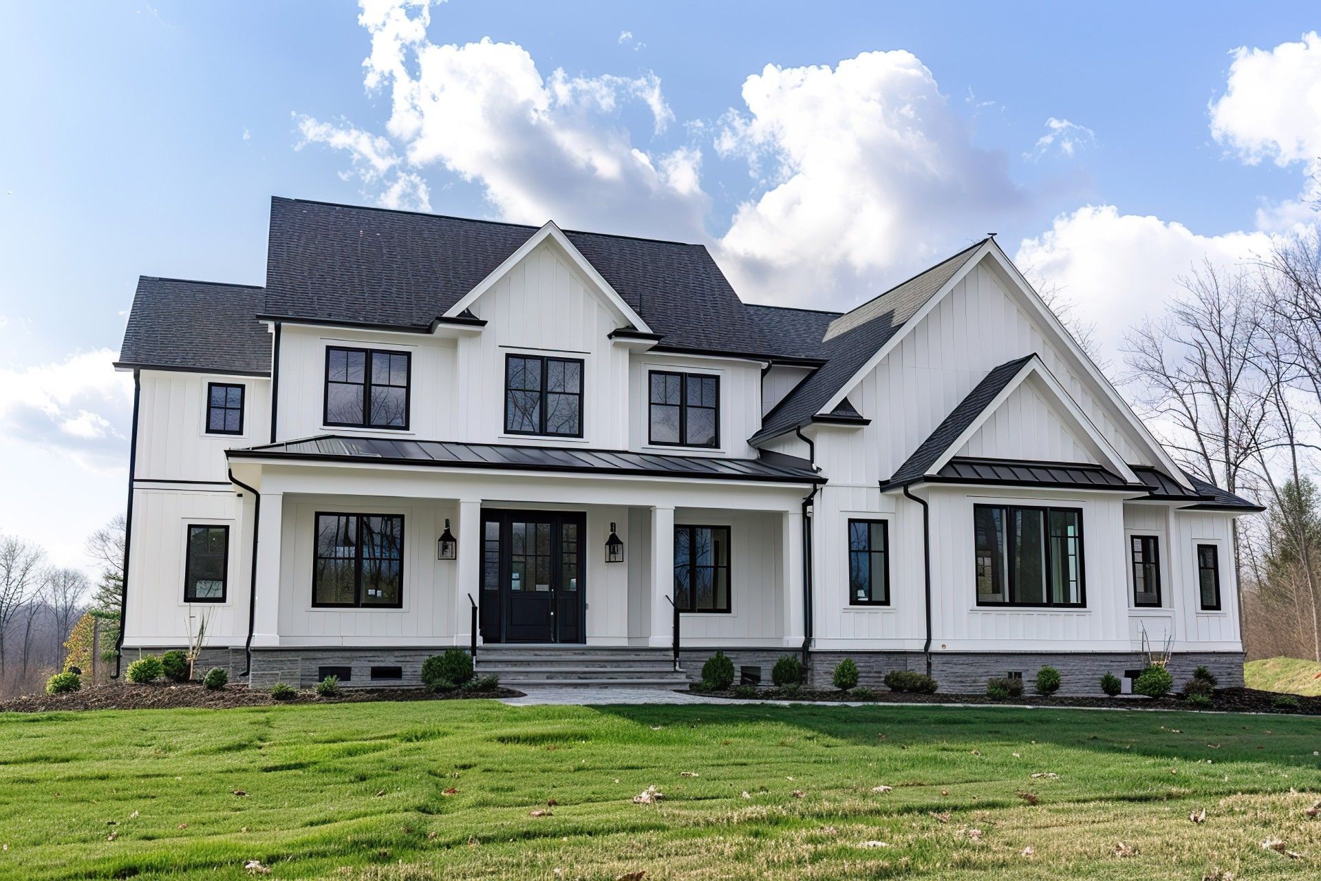 Large white two-story house with dark roof, front porch, and green lawn under a partly cloudy sky