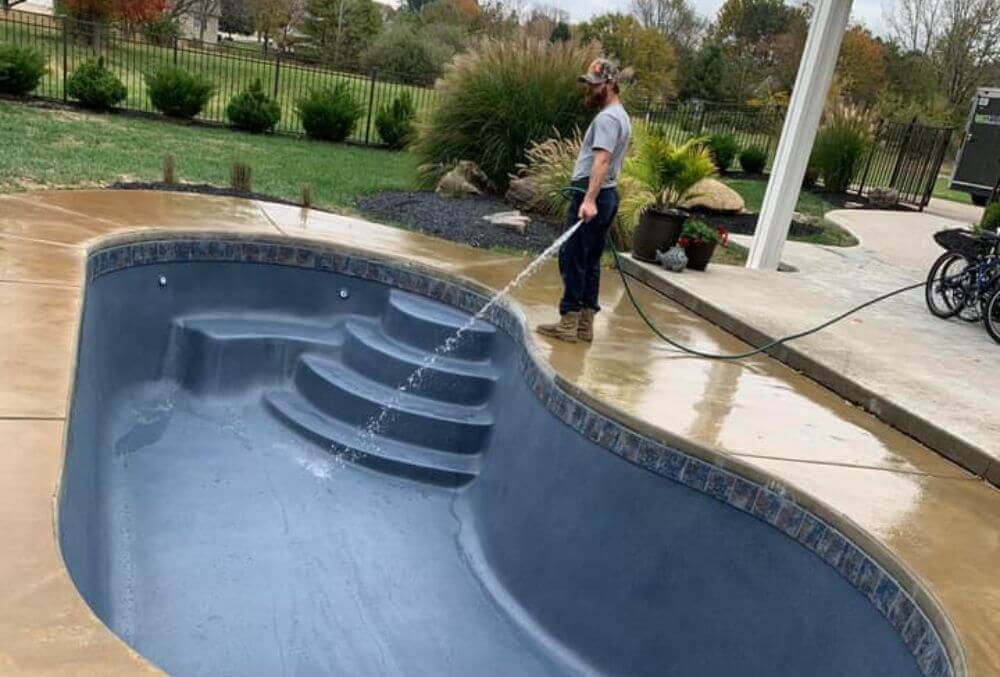 Empty custom shaped pool being cleaned by a standing man in gray shirt