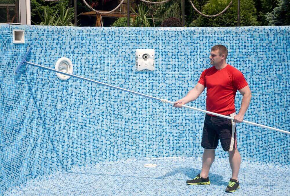 Empty pool being cleaned by a man in red shirt