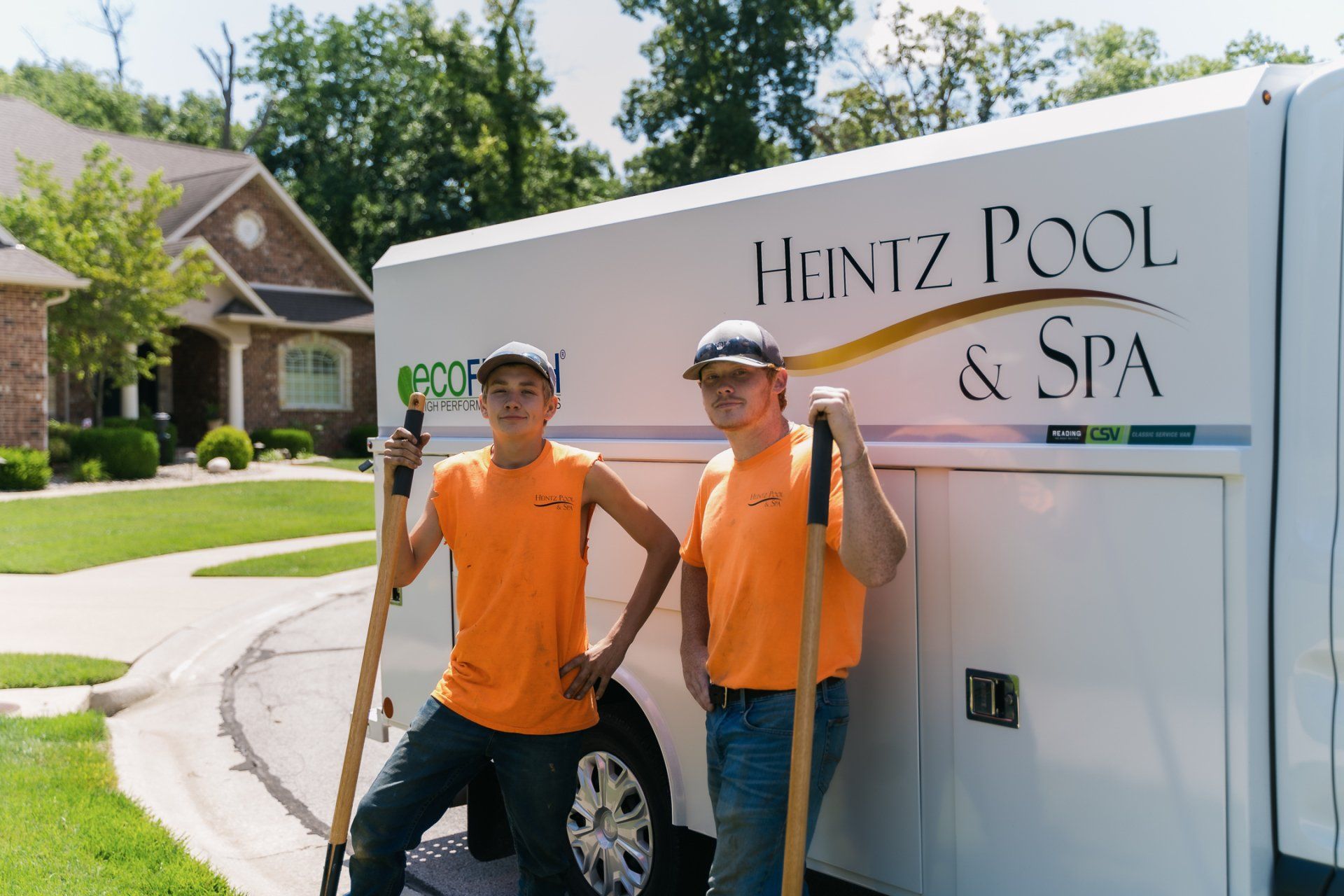 Two team members of Heintz Pool & Spa wearing orange uniform and standing with company truck as background