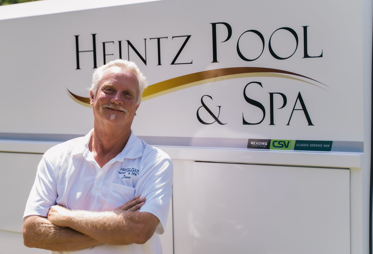 Man in white Heintz Pool & Spa uniform standing with the company truck behind him