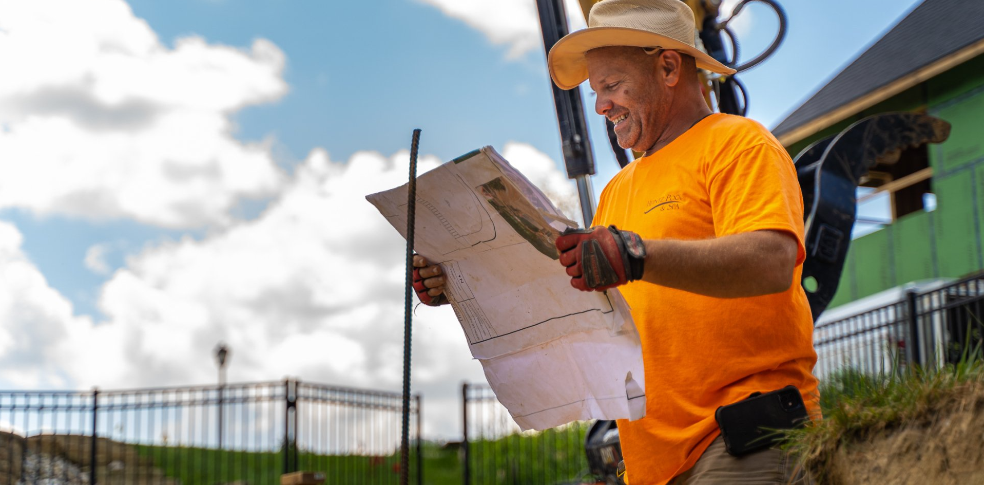 Heintz Pool & Spa worker in orange uniform happily looking at a pool construction blueprint