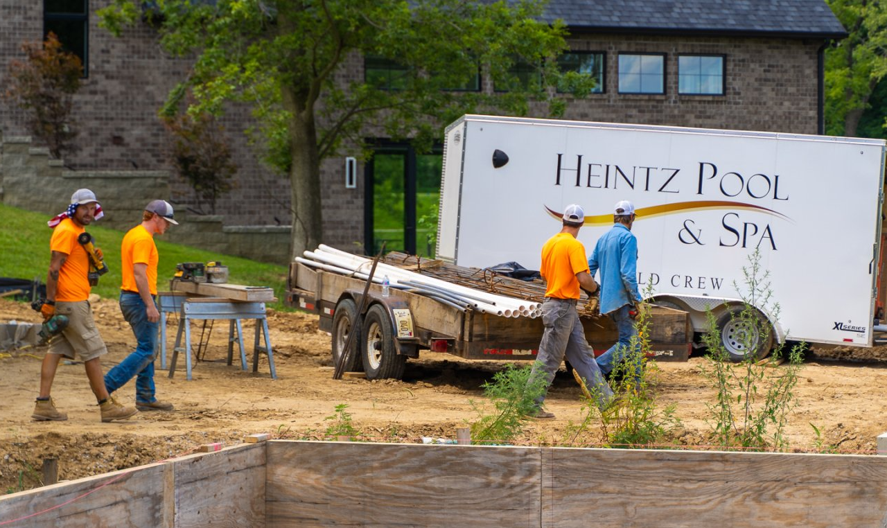 Four members of Heintz Pool & Spa walking beside an ongoing pool project with the company truck on background