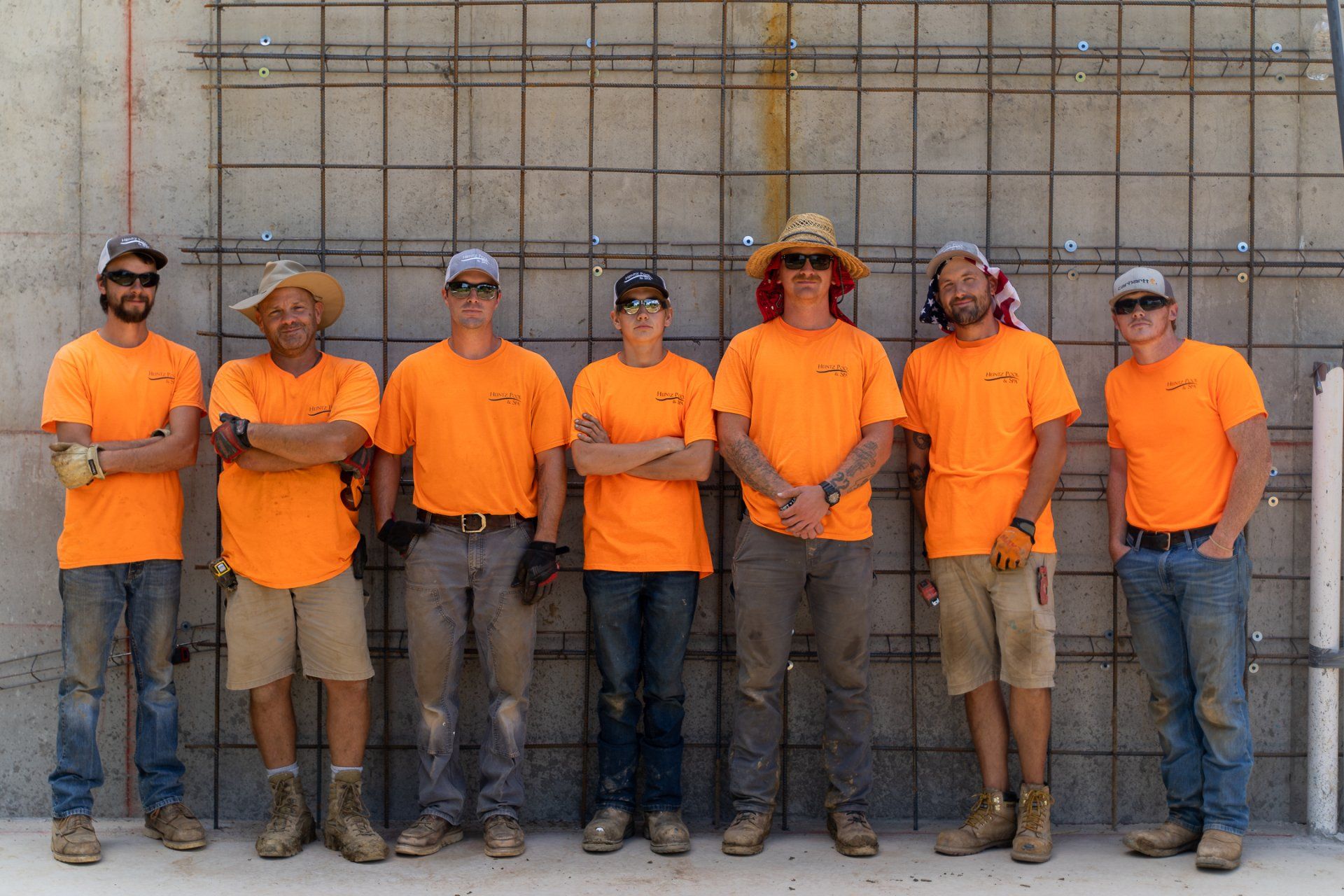 Seven members of Heintz Pool & Spa team in orange uniform standing side by side