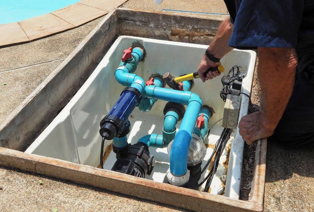 Man in blue shirt holding a tool while doing maintenance in a pool filter