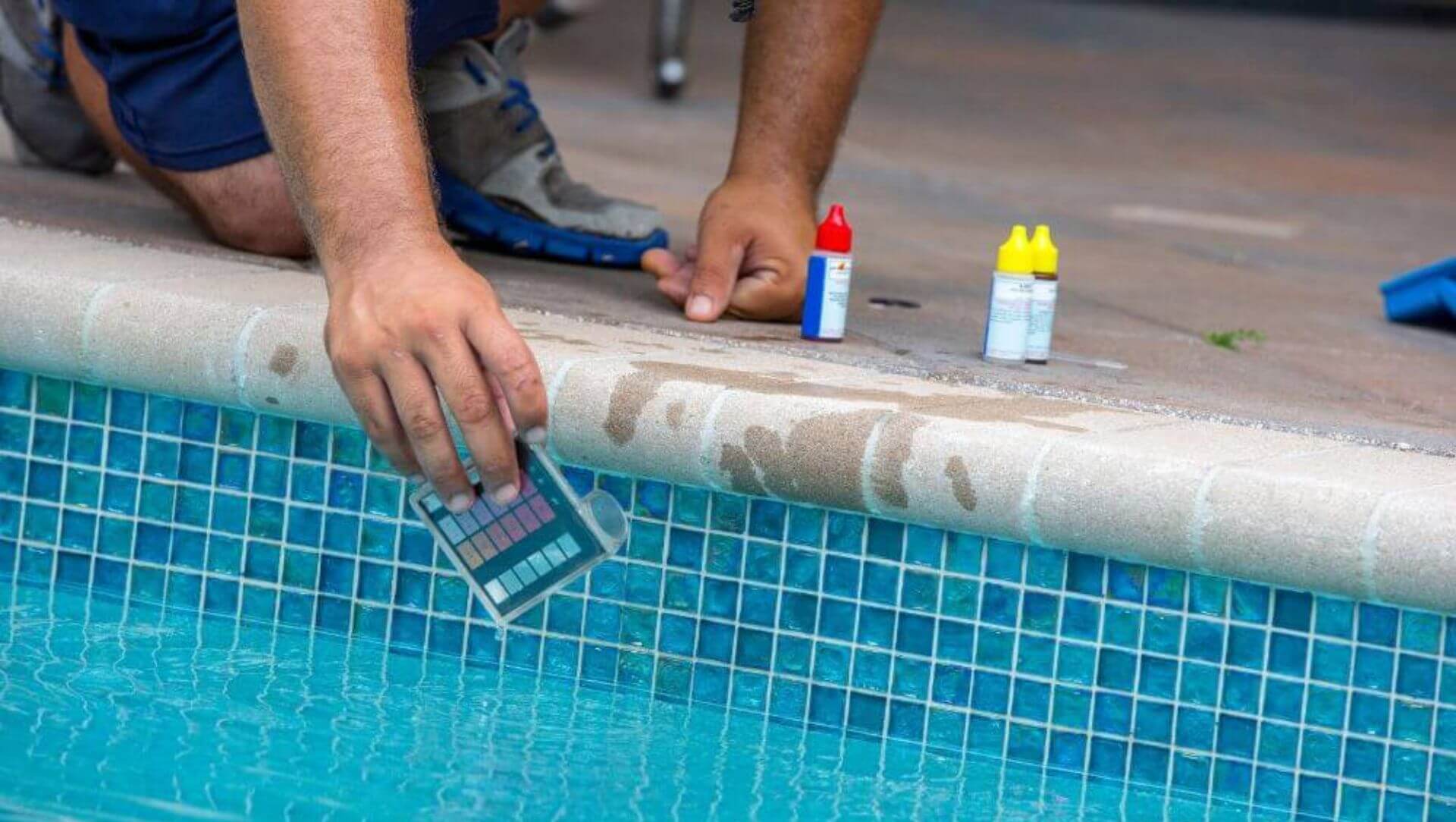 Worker in blue polo on his knees while  checking pool filters and systems