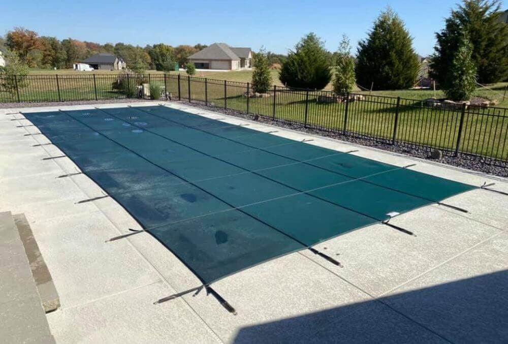 Rectangular pool with cover in a residential space with grass and trees background