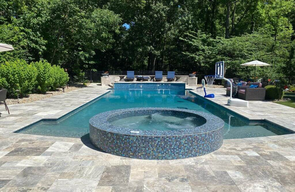 Rectangular inground pool with spa and modern concrete pool deck and trees surrounding it