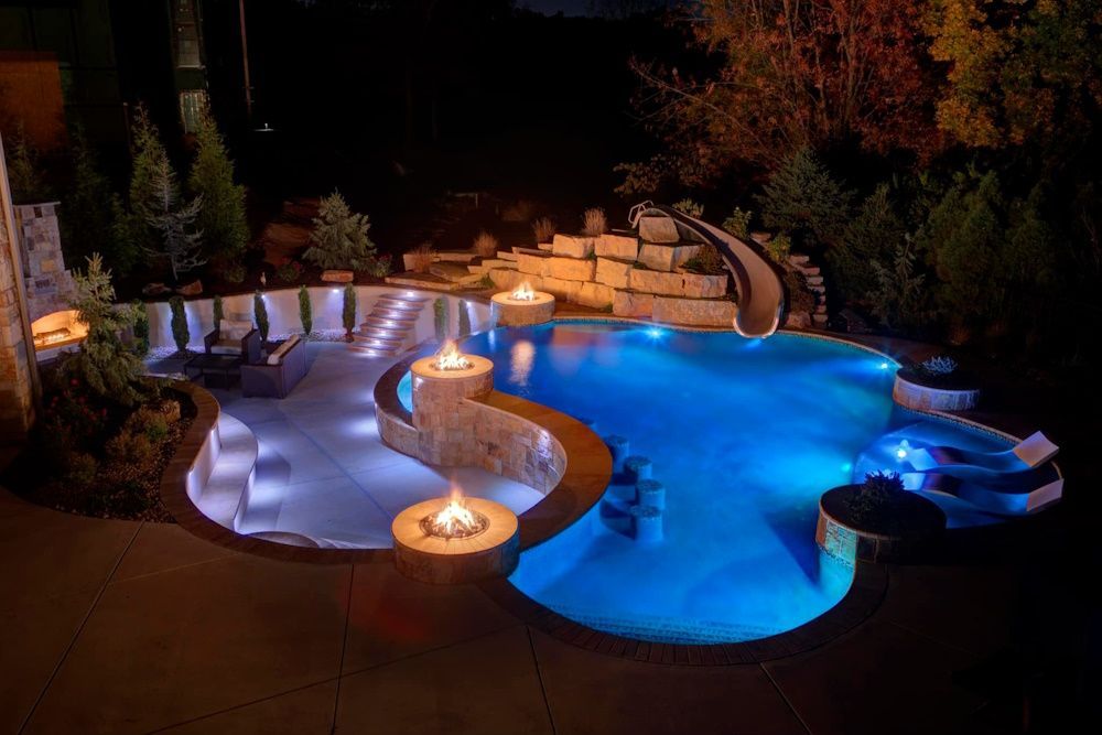 A beautiful backyard pool with a slide and fire pit at night