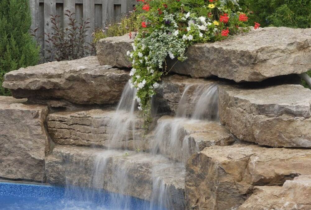 Rock waterfalls feature beside a pool with plants background