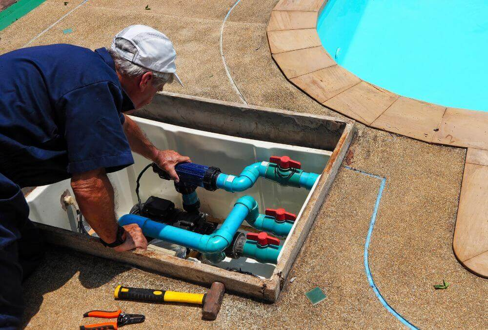 Worker in blue polo is kneeling while checking pool filters