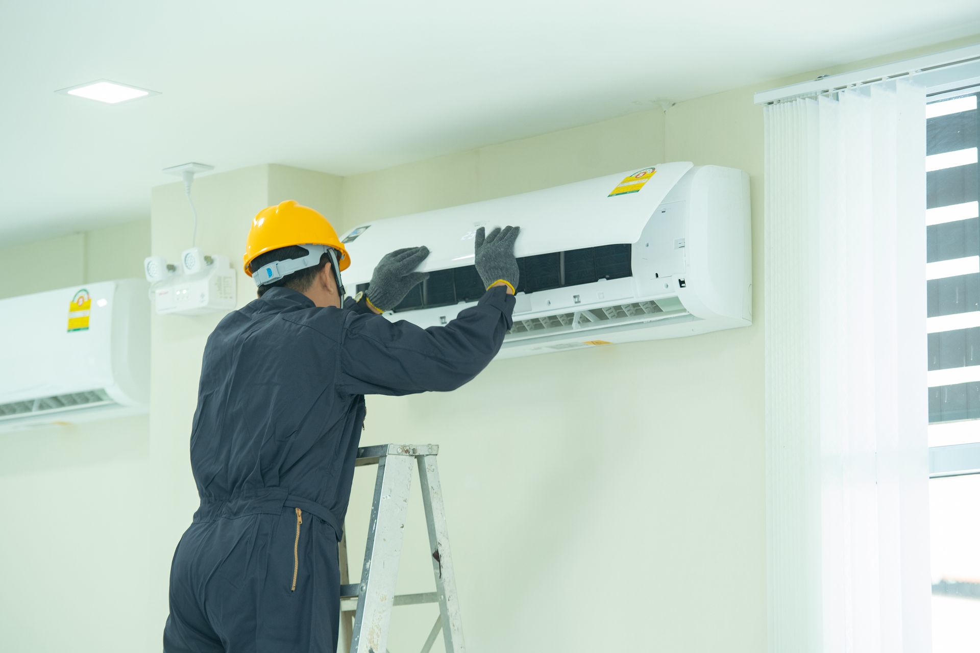 A man wearing a hard hat and overalls is doing an air conditioning installation.