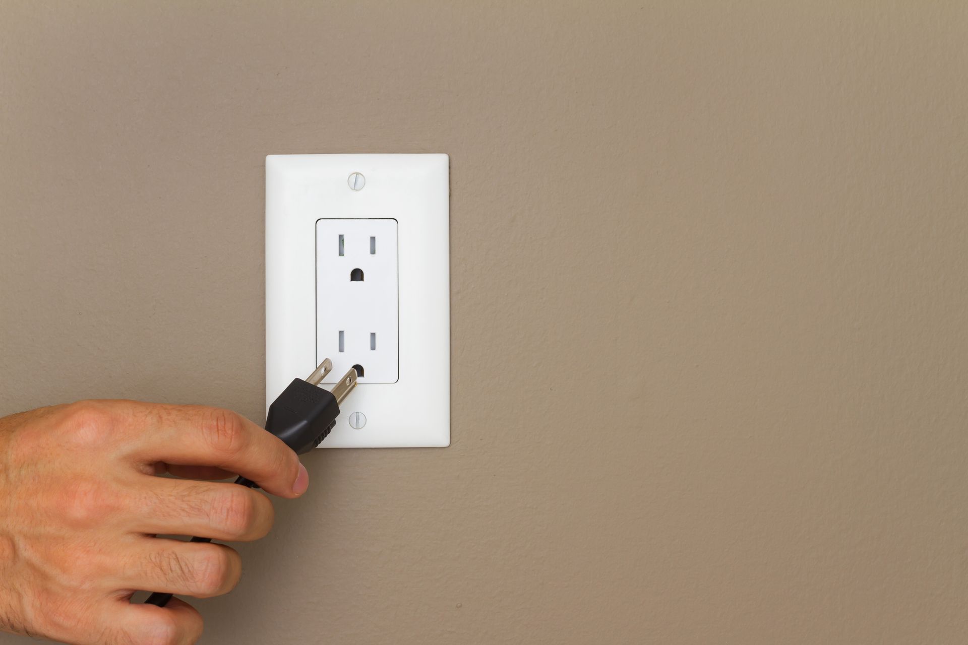 A person is plugging a cord into an electrical outlet.