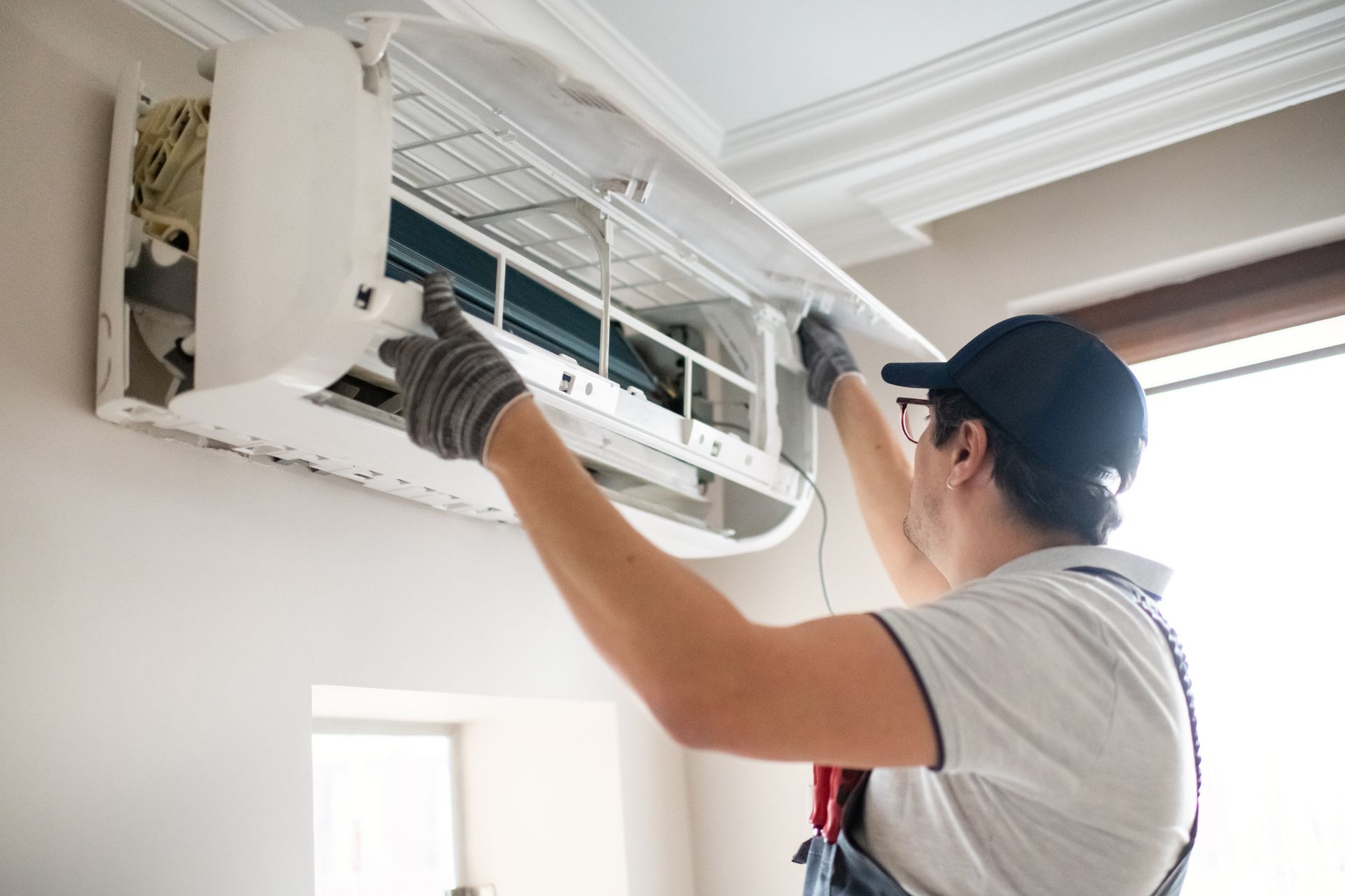Technician in blue uniform repairing wall-mounted air conditioning unit indoors.