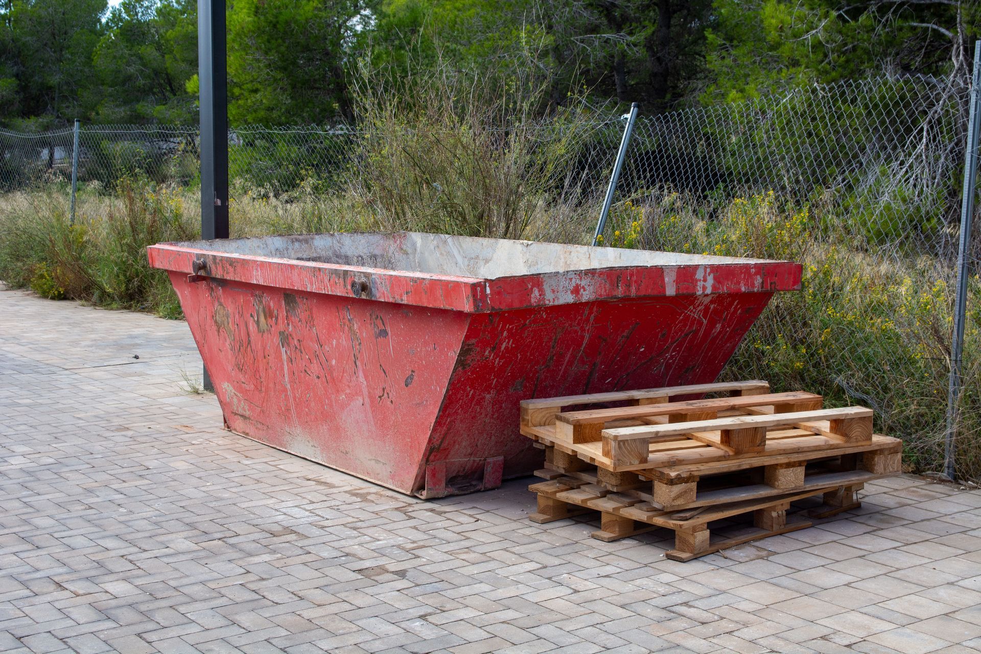 Dumpster rental featuring a red construction dumpster, highlighting stacked wooden pallets outdoors.