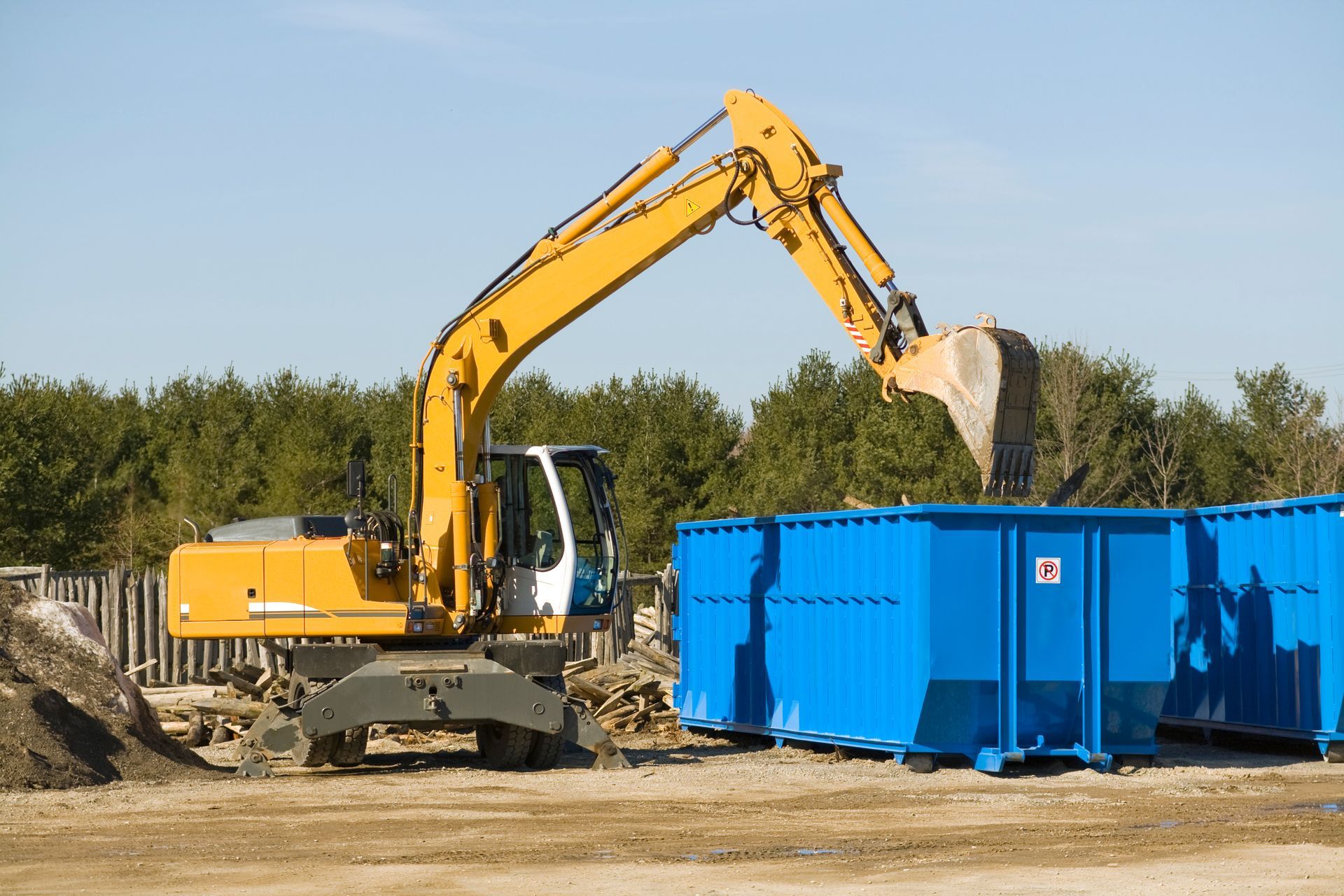 A demolition bulldozer taking debris to a blue dumpster in a construction site. A demolition bulldozer taking debris to a blue dumpster in a construction site.