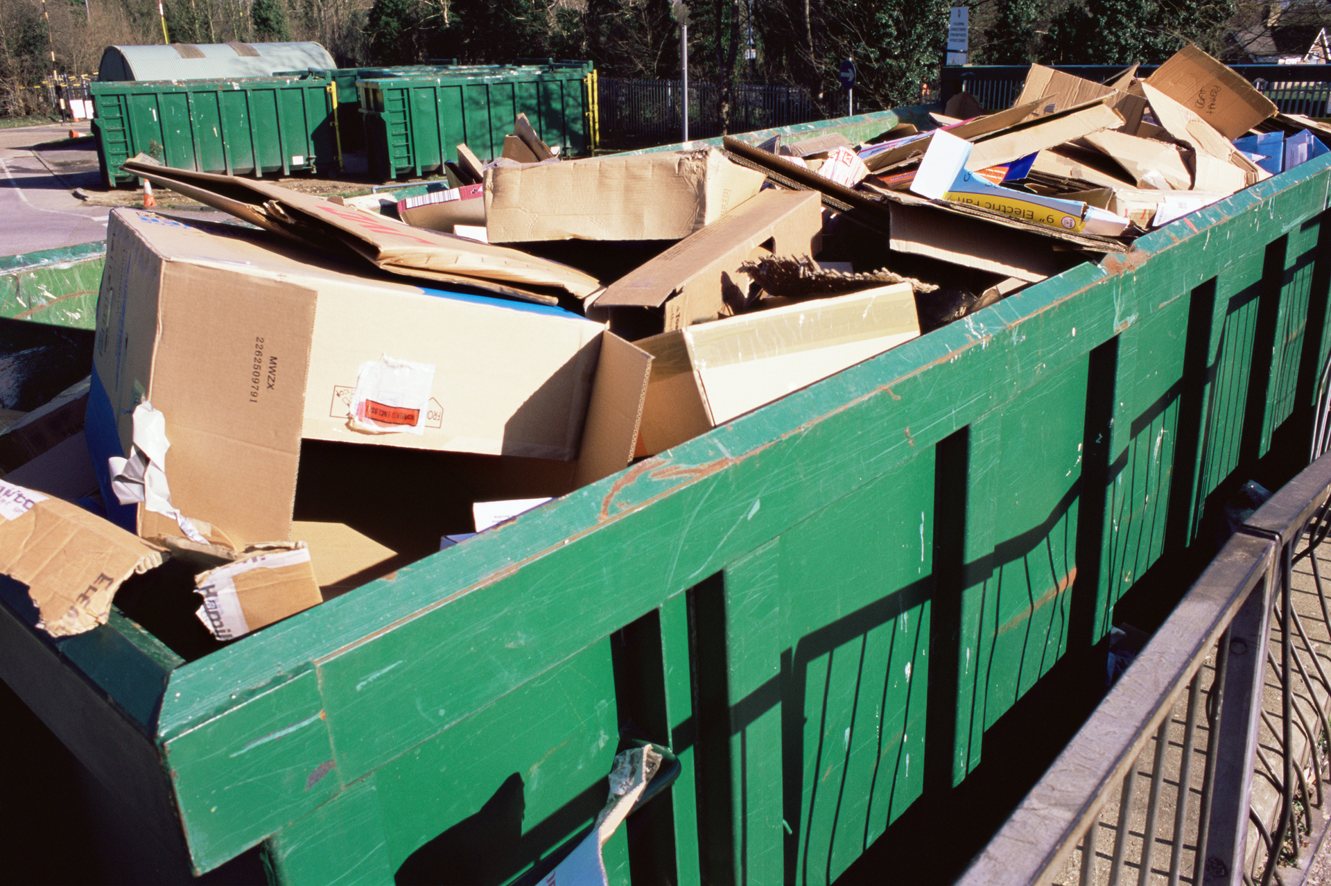 Green dumpster overflowing with flattened cardboard boxes.