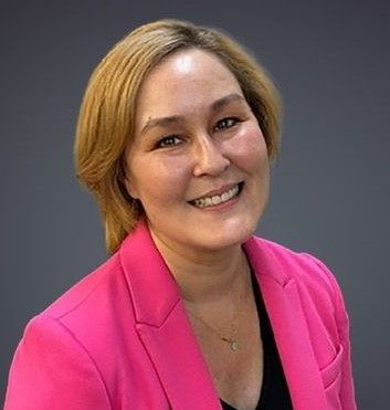 Woman with blonde hair wearing a pink blazer and black top smiles at the camera.