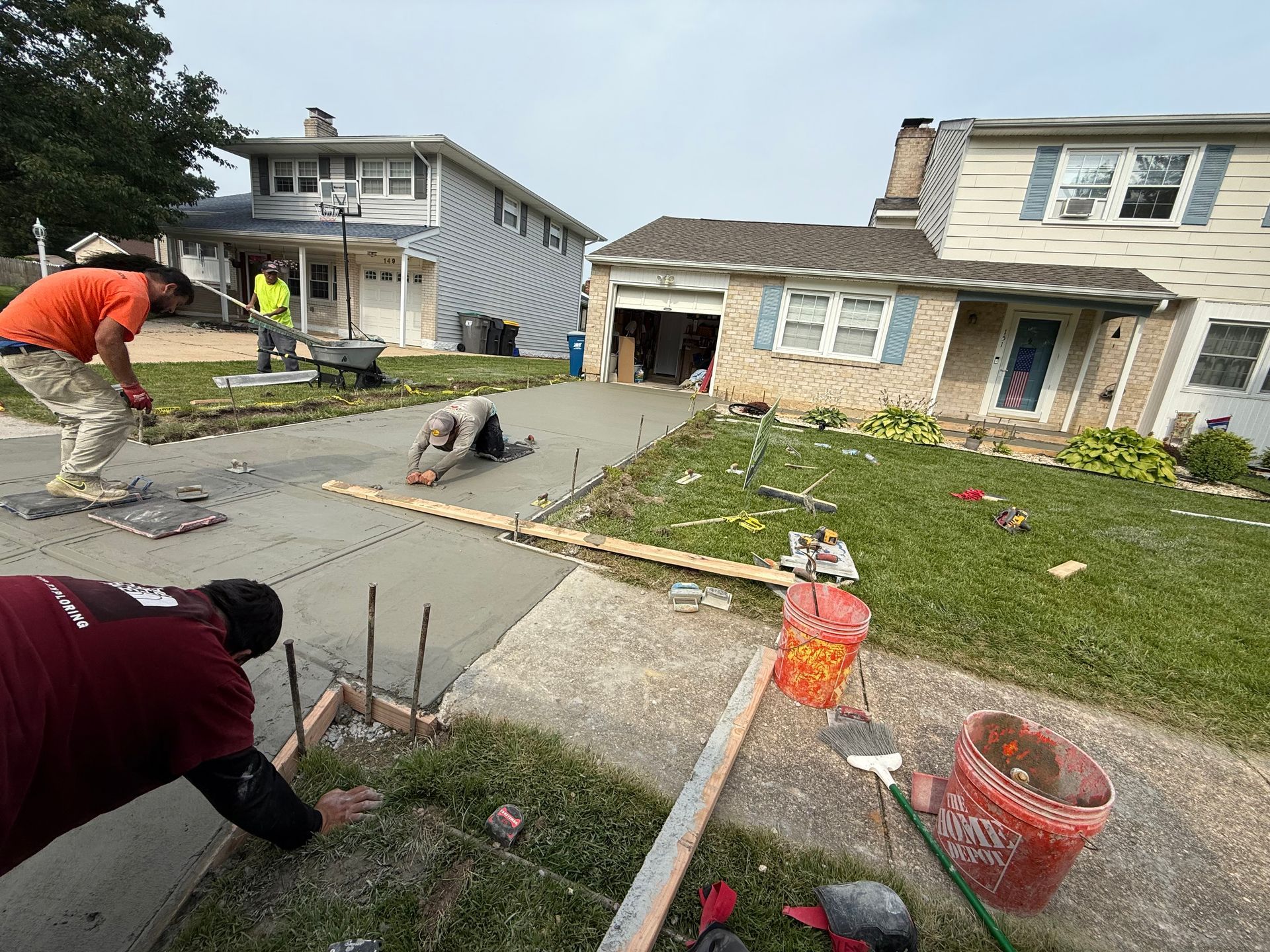 Construction workers pouring concrete for a driveway in front of a house.