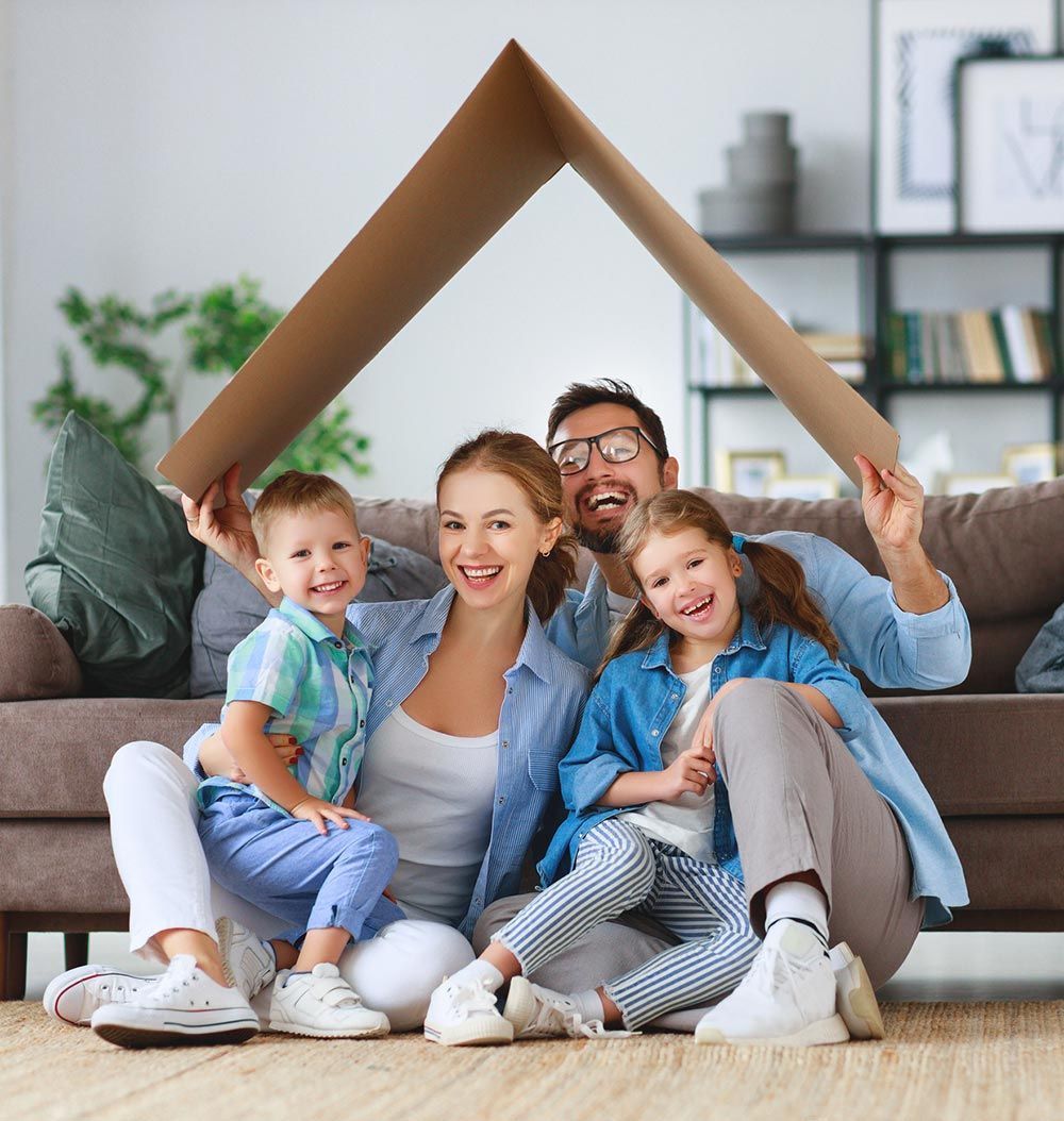 A family is sitting on a couch holding a cardboard house.