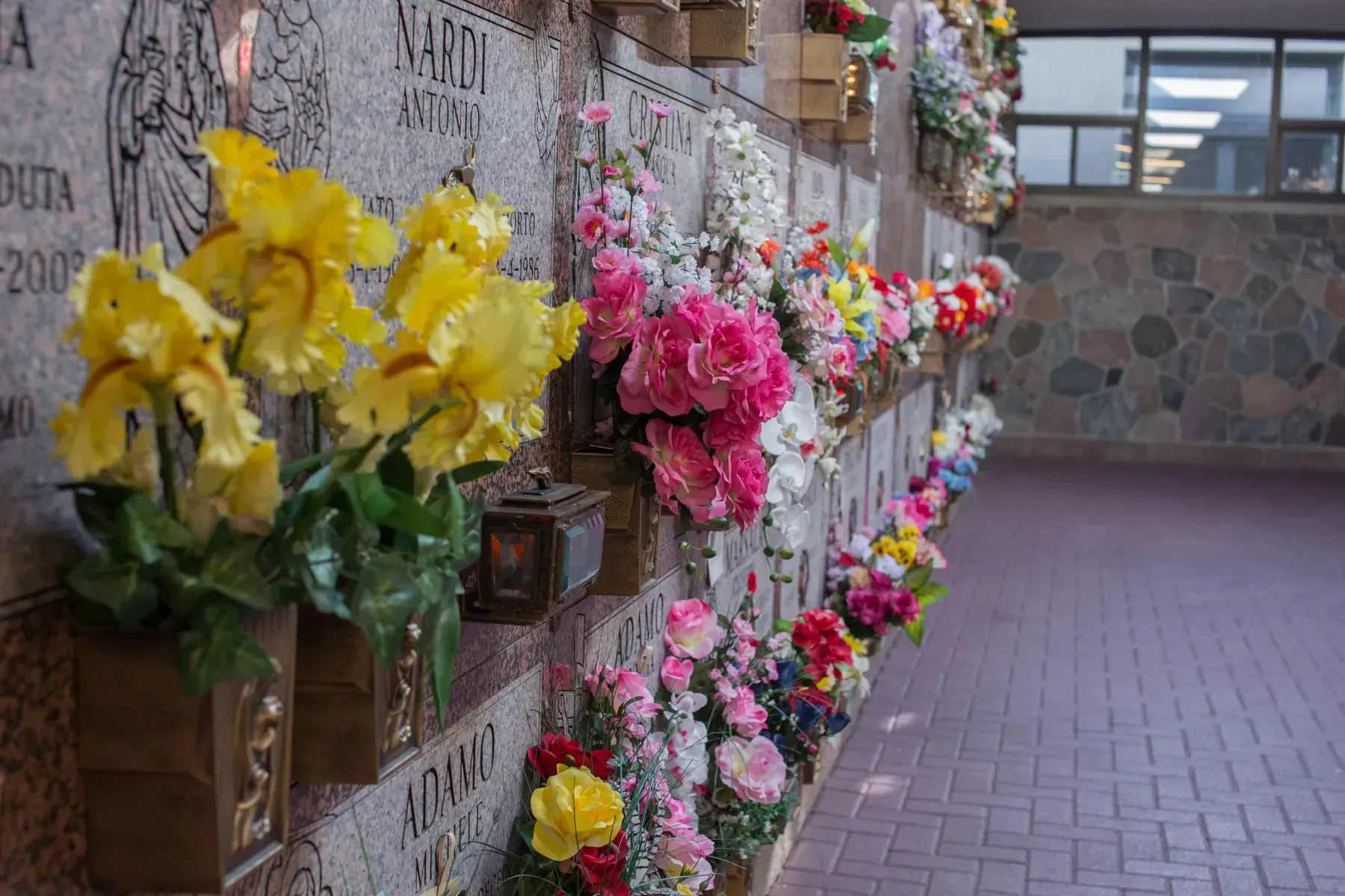 Rows of colorful flowers in wall-mounted planters along a stone corridor