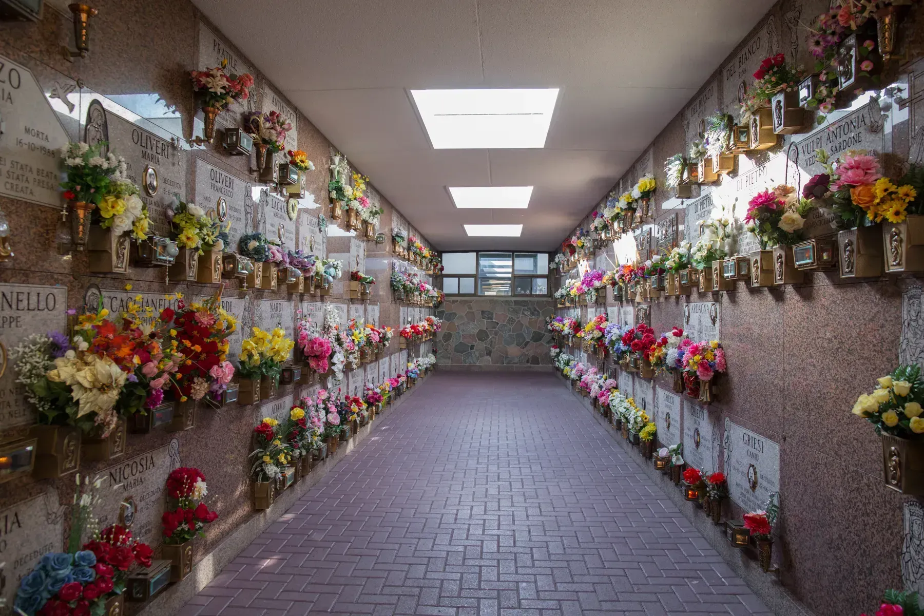 Indoor cemetery columbarium corridor lined with colorful flower-adorned memorial niches