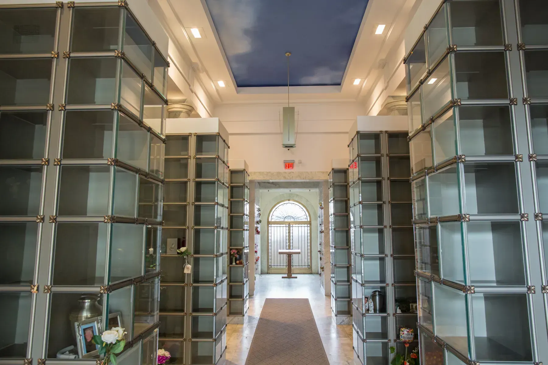 Modern columbarium corridor with glass niches, a central walkway, and a distant arched window