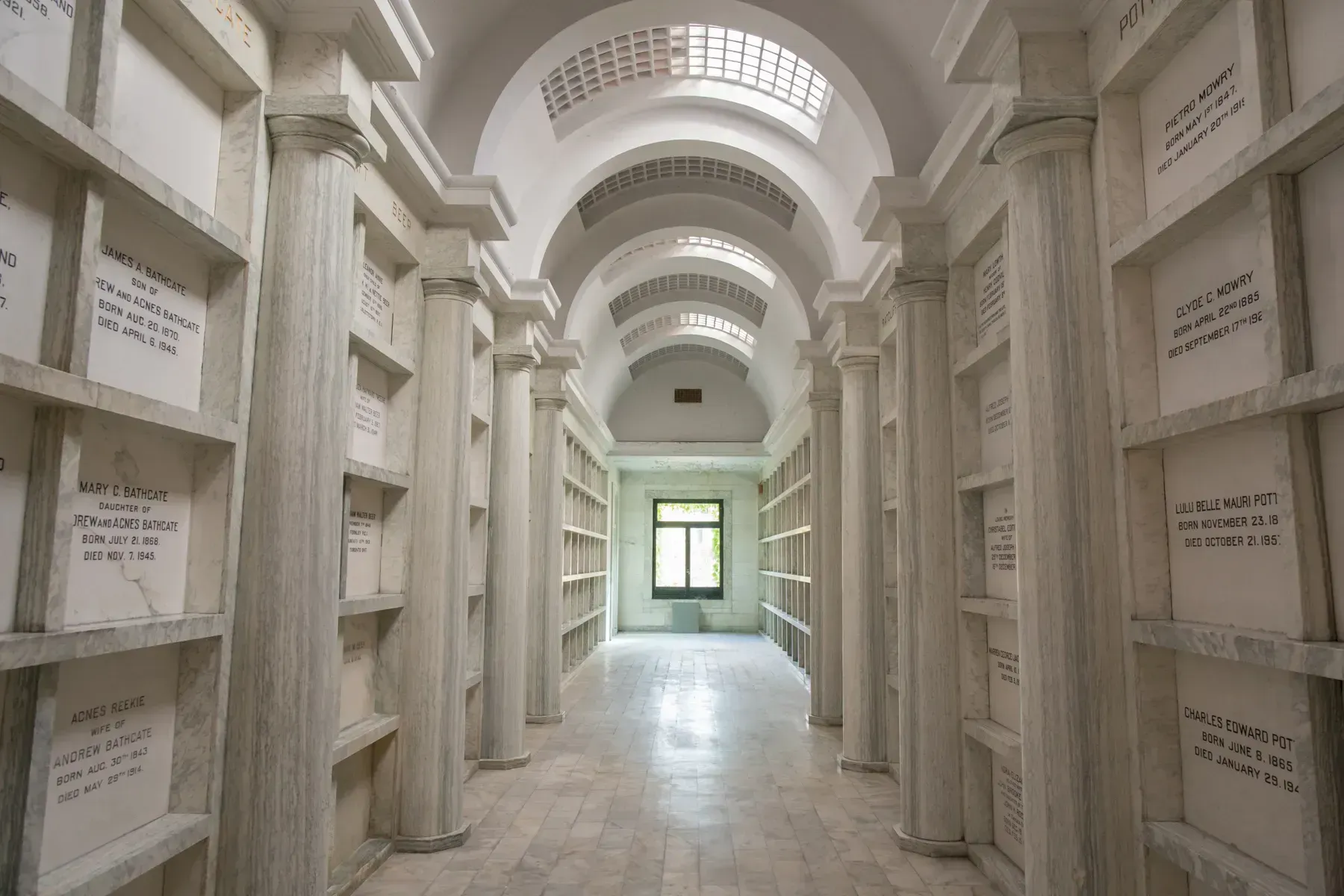 White arched mausoleum corridor with rows of niches and a bright window at the end