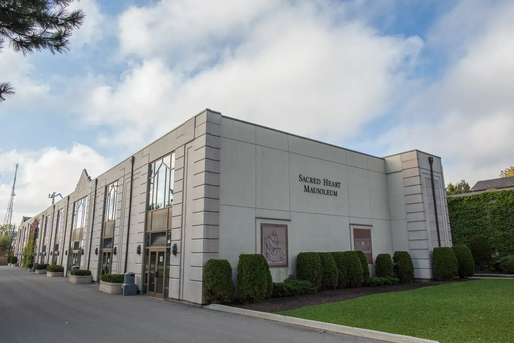 Modern stone office building with large windows, landscaped shrubs, and cloudy sky
