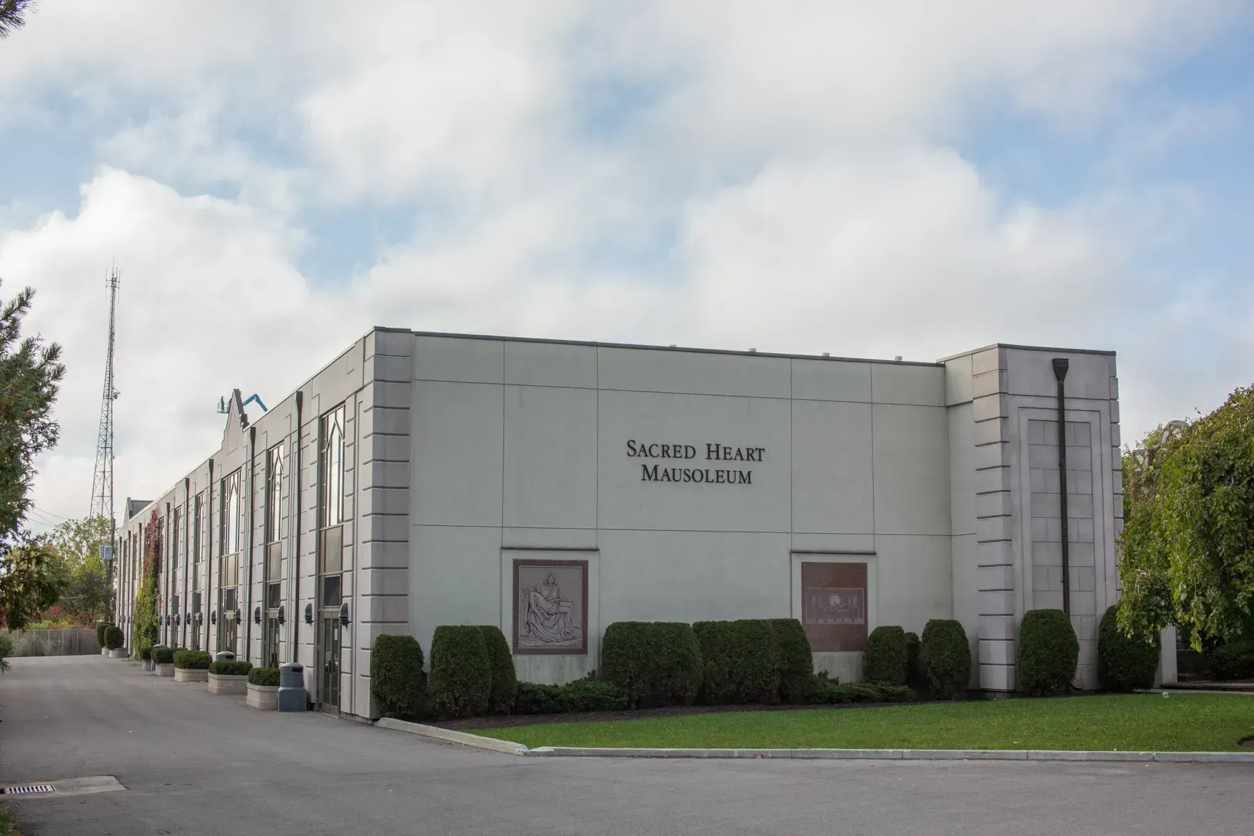 Exterior of a white funeral home building with trimmed hedges and a partly cloudy sky