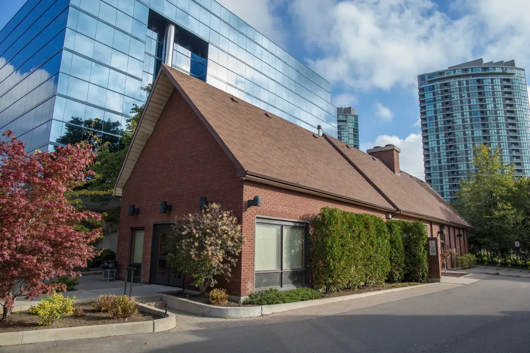 Brick building with a steep roof beside a modern glass high-rise under a blue sky.