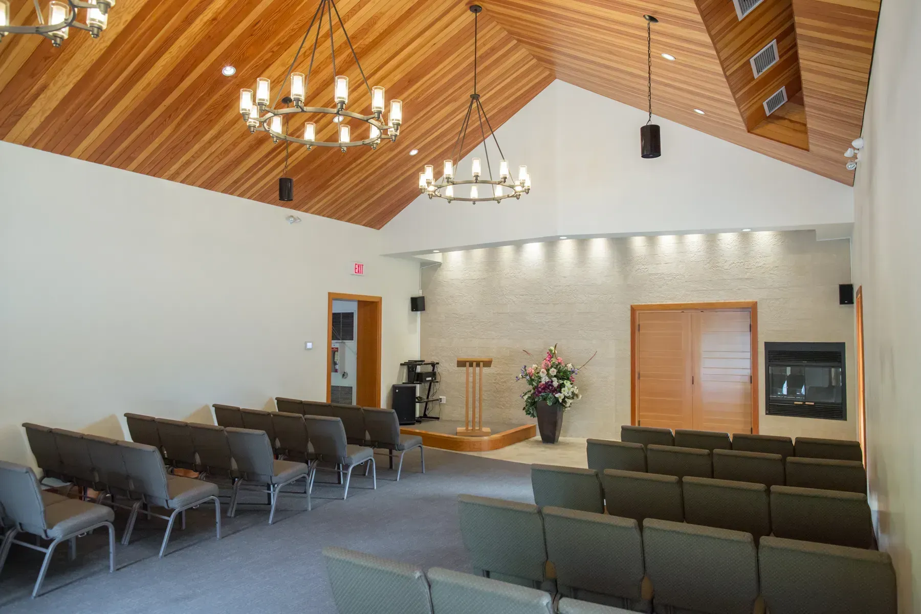 Empty church sanctuary with rows of chairs, wood-paneled ceiling, chandeliers, and a pulpit at the front