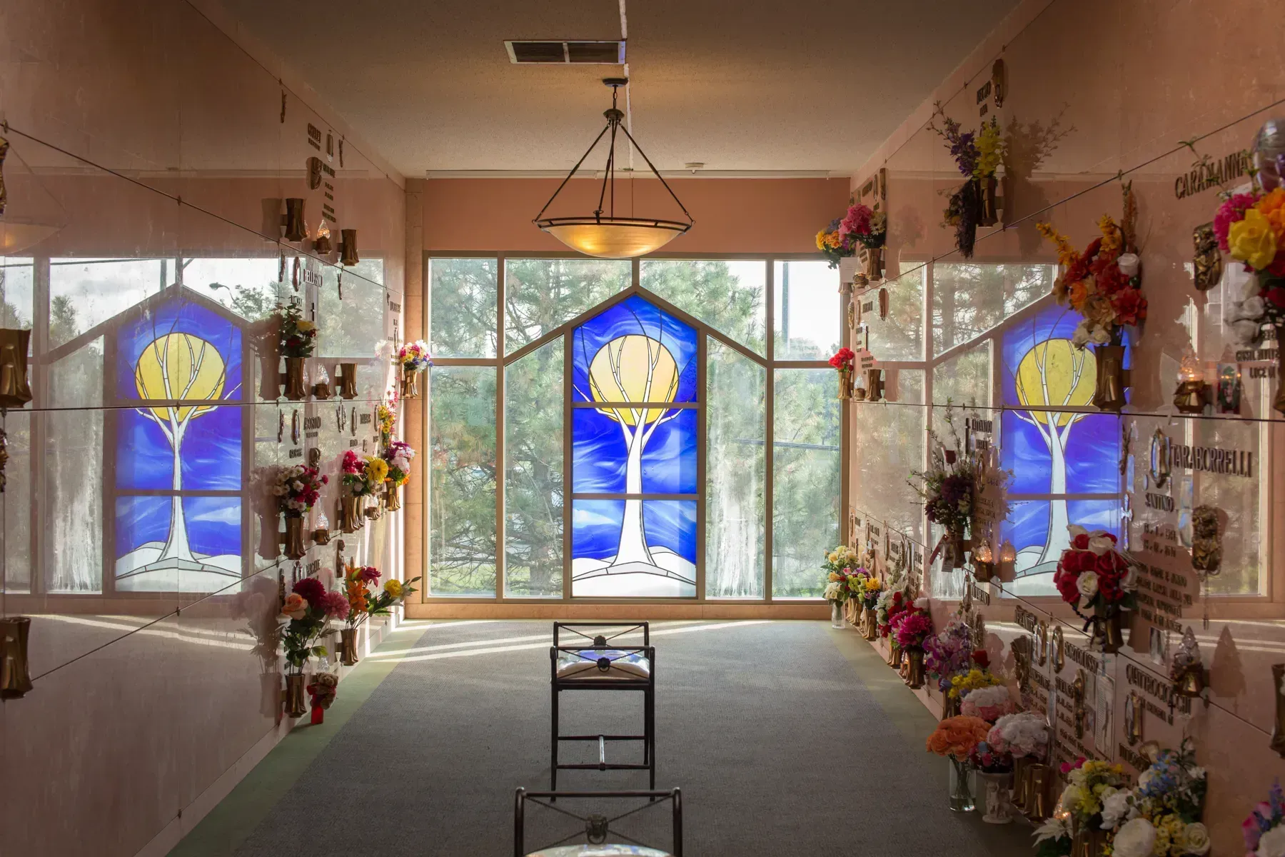 A flower-filled chapel with stained-glass windows and sunlight streaming through the center.