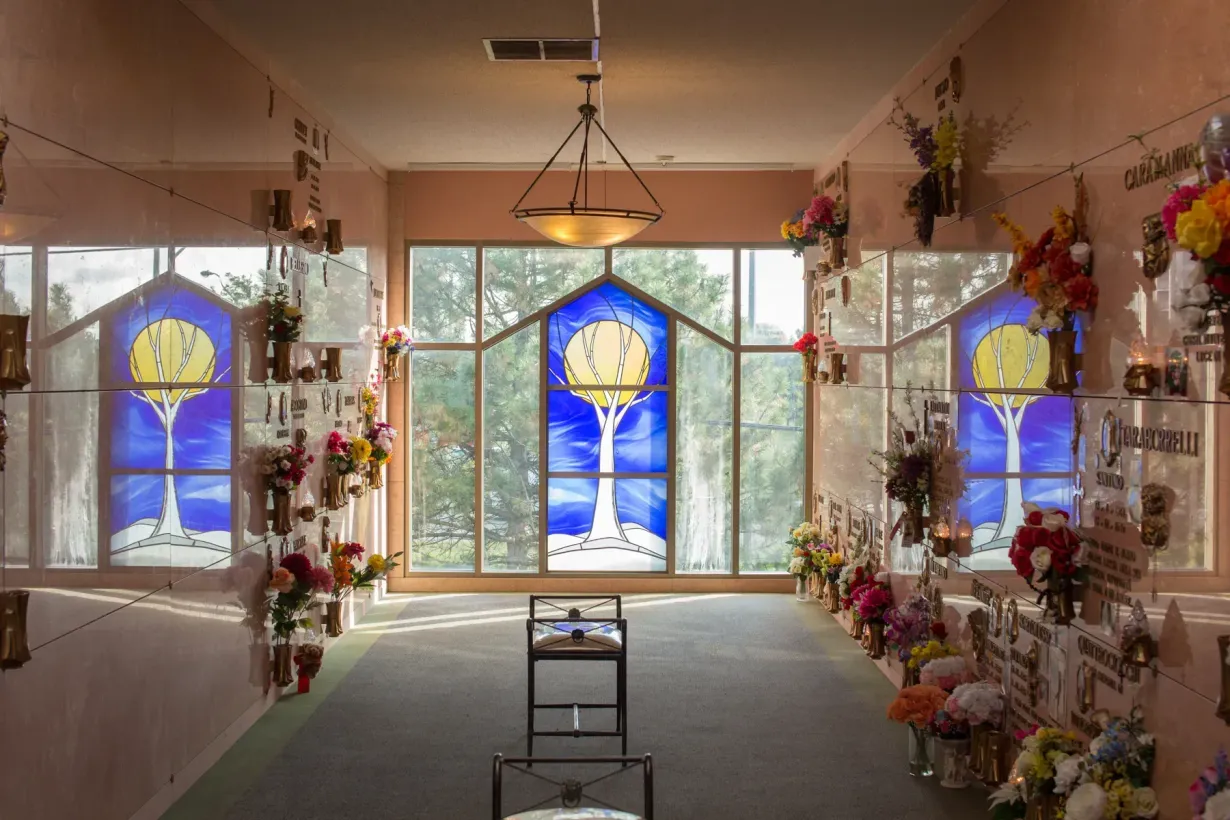 Decorated indoor memorial altar with flowers and stained-glass windows at the back