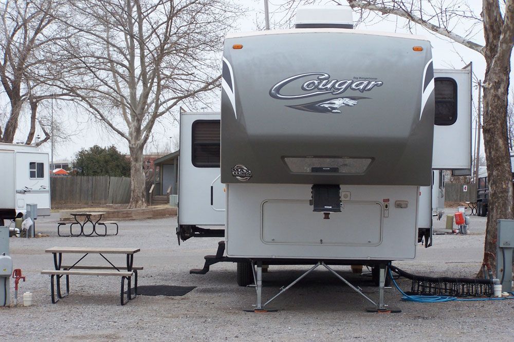 A cougar trailer is parked in a gravel lot next to a picnic table.
