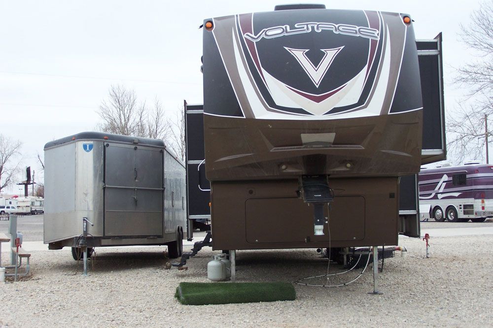 A rv is parked next to a trailer in a gravel lot.