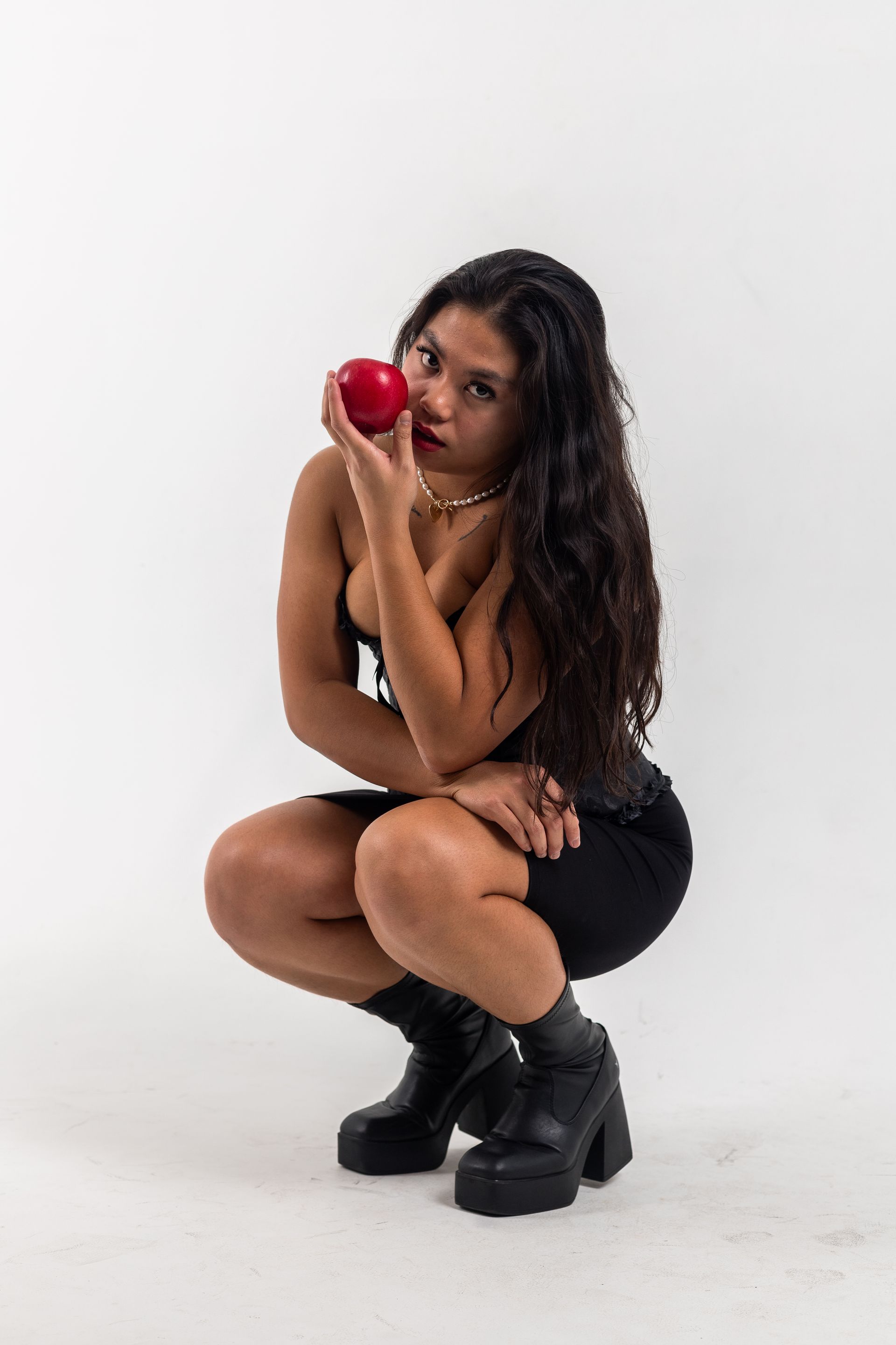 a woman is squatting down while holding a red apple in her hand .