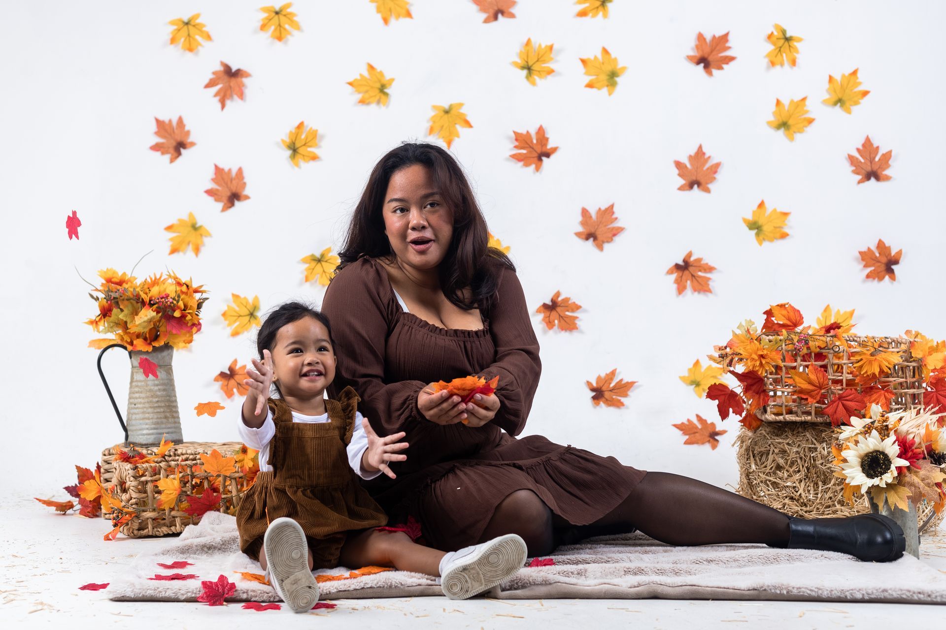 a woman and a little girl are sitting on the floor in front of a wall of leaves .