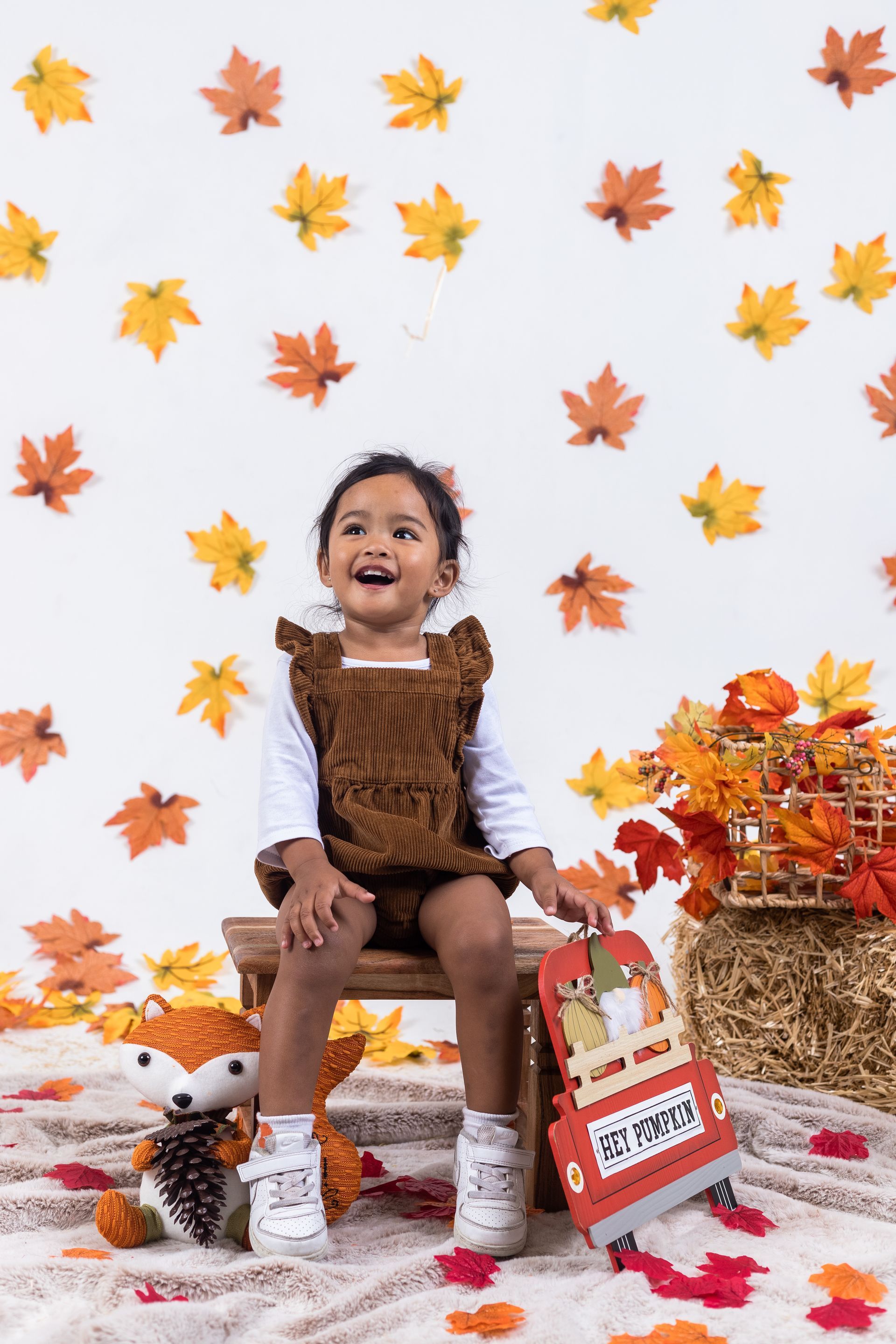 a little girl is sitting on a stool in front of a wall of leaves .