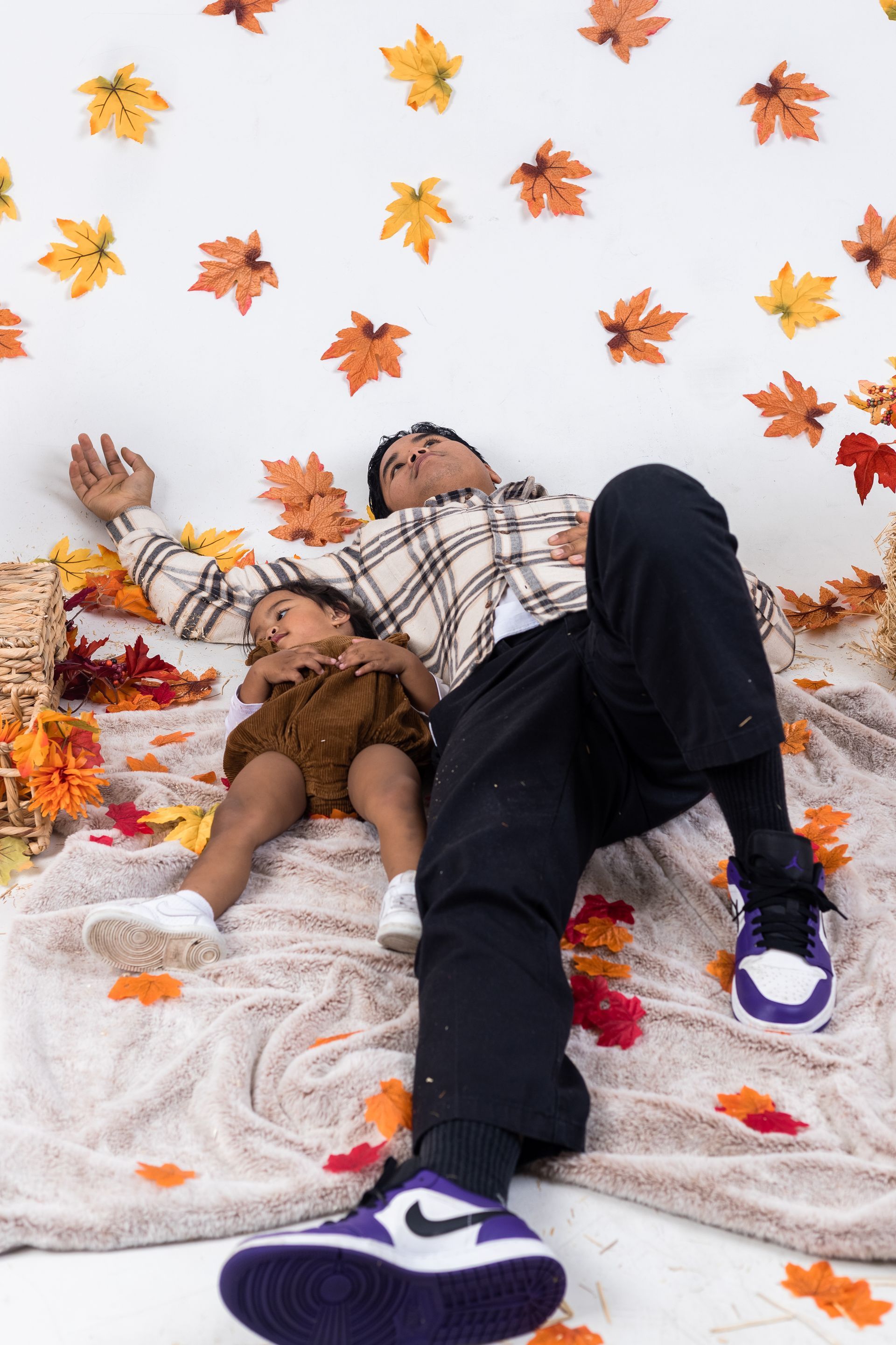 a man and a child are laying on a blanket surrounded by leaves .