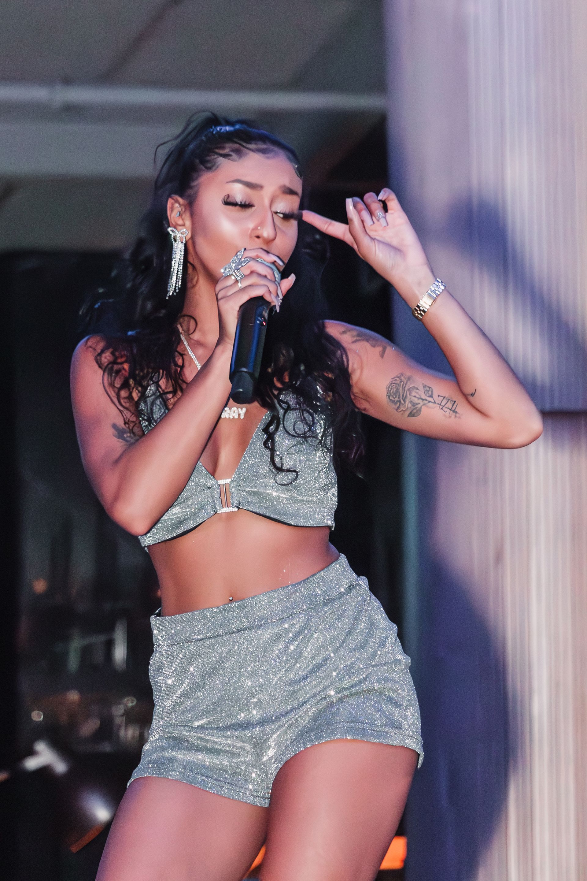 a woman in a crop top and shorts is singing into a microphone .