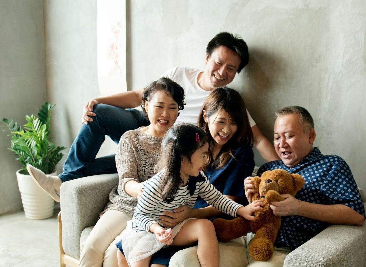 A family is sitting on a couch playing with a teddy bear.