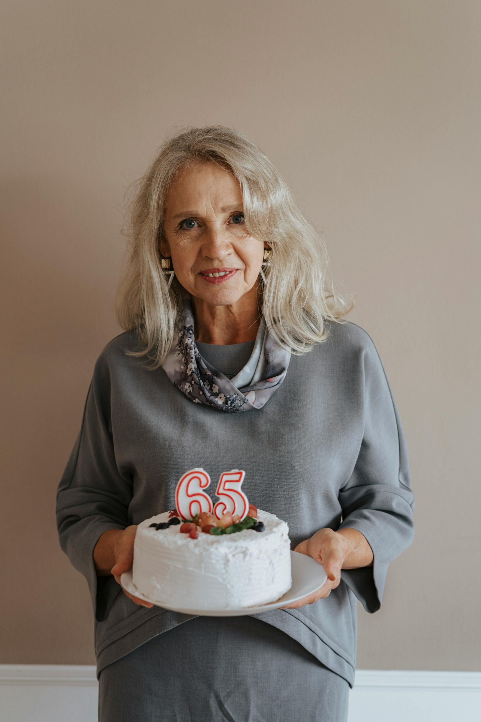 An elderly woman is holding a birthday cake with candles on it.