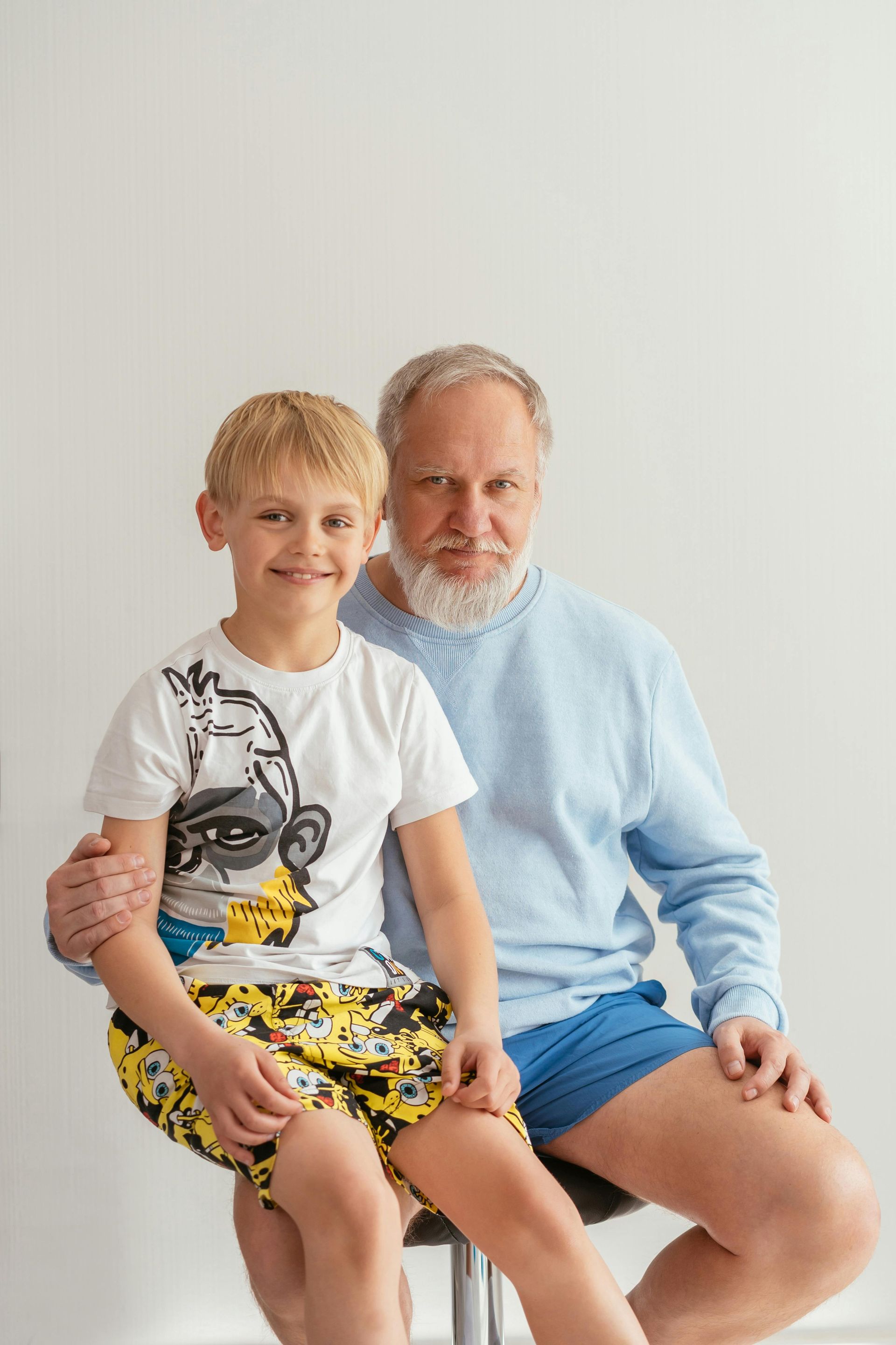 An elderly man and a young boy are sitting on a stool.